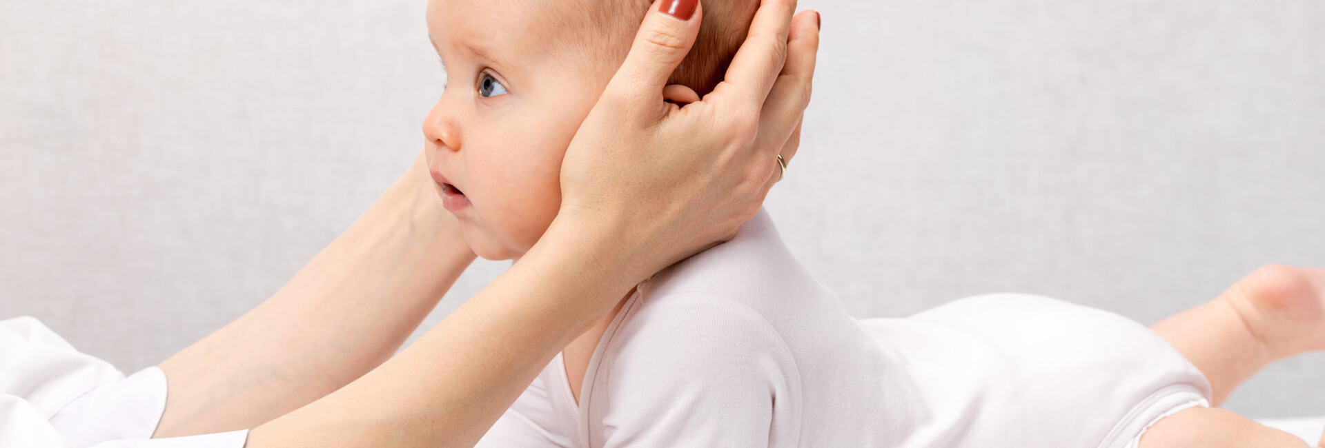 Six month baby girl receiving osteopathic or chiropractic treatment in pediatric clinic. Manual therapist manipulates chils's head and neck